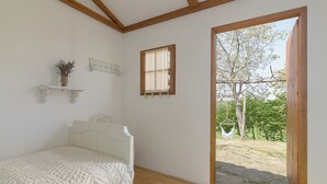 Een slaapkamer met een bed, een klein raam en uitzicht op een buitenruimte met bomen.