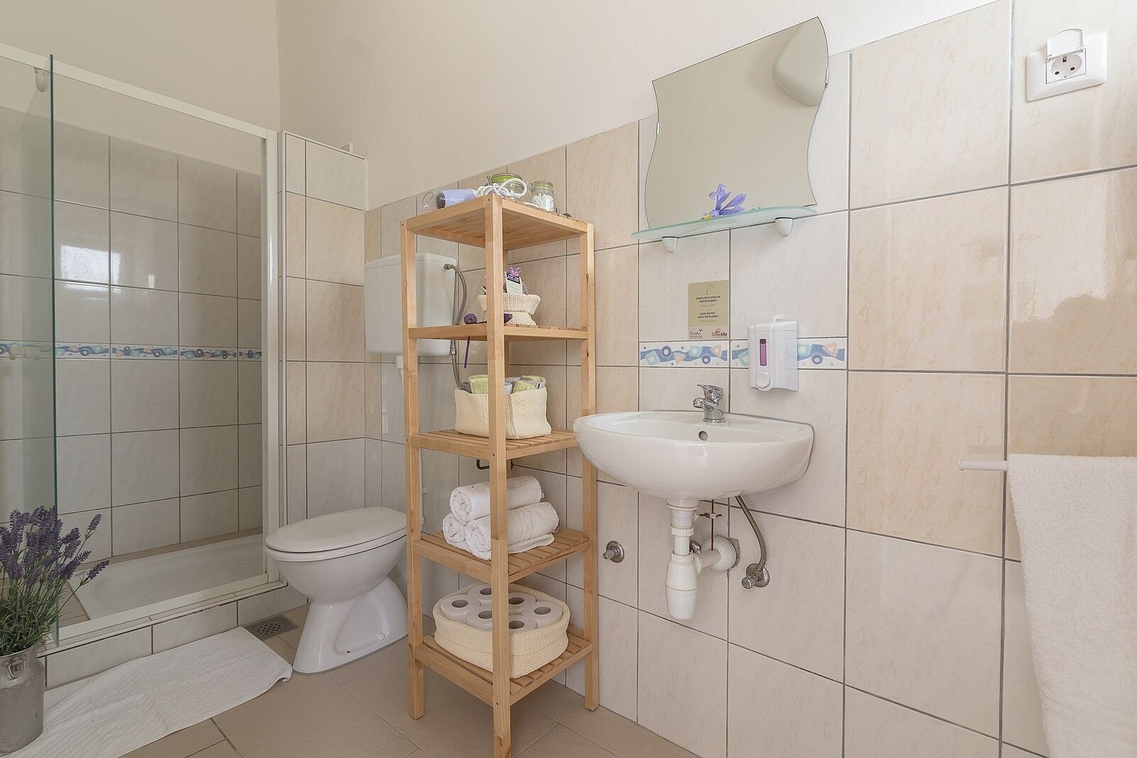 A bathroom with a toilet, sink, and a wooden shelf with towels and toiletries.