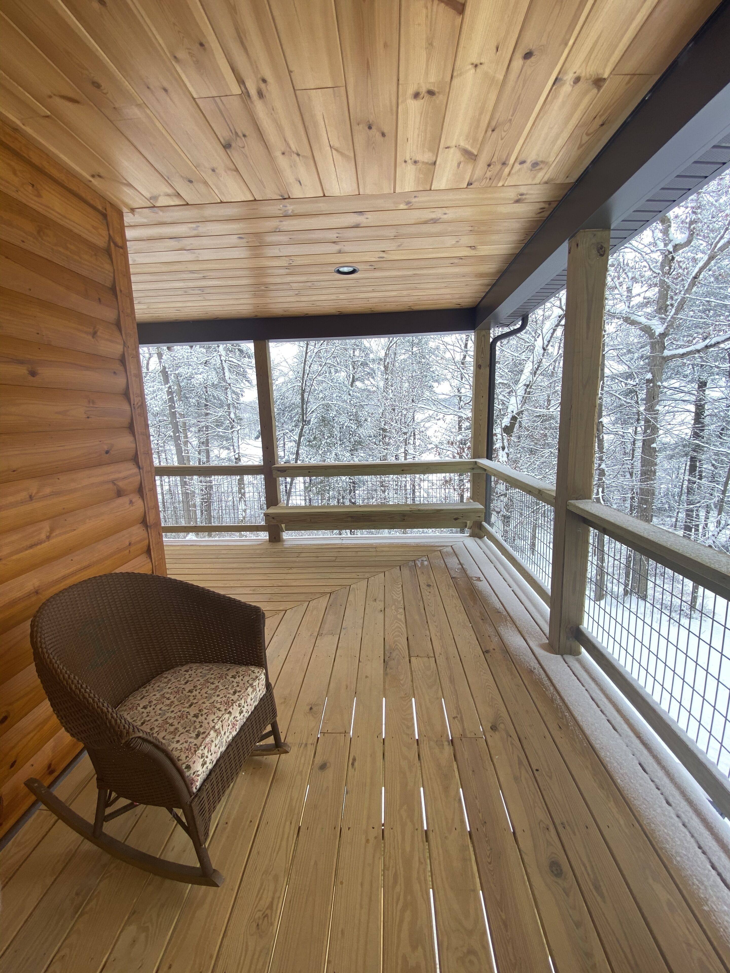 En träveranda med en gungstol, träväggar och utsikt över snötäckta träd.