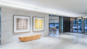 A modern lobby with marble flooring, framed artwork, a wooden bench, and a glass elevator entrance. - Ji Hotel(shanghai Hongqiao Trans Hub Xujing Branch (Shanghai)