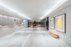 Eine moderne Hotelhalle mit Empfangstresen, Sitzgelegenheiten und gerahmten Kunstwerken an den Wänden.