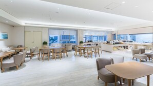 A modern hotel dining area with multiple seating arrangements, a kitchen area, and large windows providing views. - Ji Hotel(shanghai Hongqiao Trans Hub Xujing Branch (Shanghai)