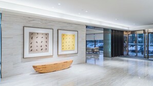 Eine moderne Lobby mit Marmorböden, gerahmten Kunstwerken, einer hölzernen Bank und einem Eingang zu einem gläsernen Aufzug.