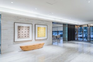 A modern lobby with marble flooring, framed artwork, a wooden bench, and a glass elevator entrance. - Ji Hotel(shanghai Hongqiao Trans Hub Xujing Branch (Shanghai)