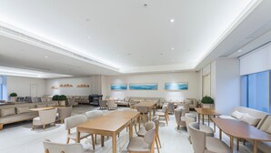 Eine großzügige Hotelhalle mit verschiedenen Sitzbereichen, darunter Sofas und Tische, und einem großen Fenster, das für natürliches Licht sorgt.