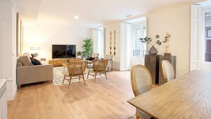 Ein geräumiges Wohnzimmer mit einer Couch, einem Esstisch, Stühlen, einem Flachbildfernseher und einer Topfpflanze.