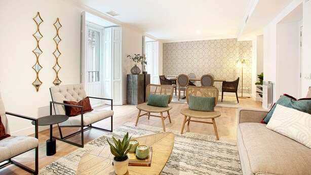 Ein modernes Wohnzimmer mit einer Couch, Sesseln und einem Couchtisch. Im Hintergrund ist ein Essbereich mit Tisch und Stühlen zu sehen.