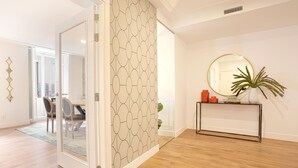 A modern interior with a wooden floor, a glass door leading to a dining area, a round mirror on a console table, and a patterned wall. - Genteel Home Madrazo I (Madrid)