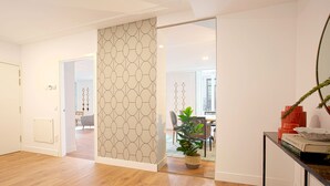 Ein modernes Interieur mit Holzboden, einer verzierten Schiebetür, einem Essbereich mit Stühlen und Tisch sowie einer kleinen Pflanze auf einer Konsole.