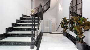 Uma escadaria de mármore com grades pretas que dá acesso a um elevador.
