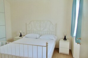 A single-bed room with a white metal headboard, two bedside tables with lamps, and a door with a curtain.