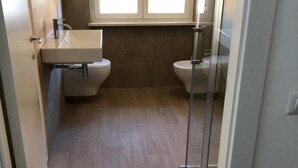 Ein kleines Badezimmer mit Waschbecken, zwei Toiletten und einem Fenster.