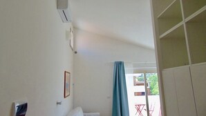 Quarto com cama, janela com cortina, ar-condicionado na parede e vista para o exterior.