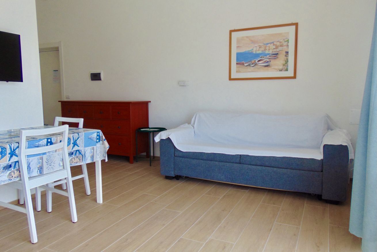 A living room with a blue sofa, a white table with a patterned tablecloth, a red cabinet, and a framed painting on the wall.