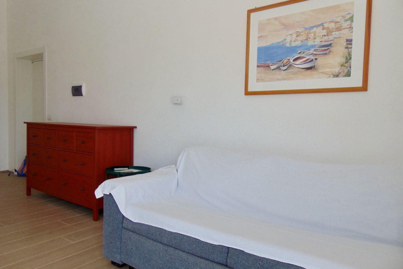 A room with a bed, a red dresser, and a framed painting on the wall.