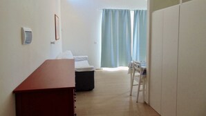 Quarto com escrivaninha de madeira, cama, cadeira, guarda-roupa e janela com cortinas.