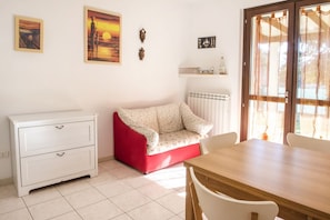 A room with a white dresser, a red sofa, a wooden dining table, and a window with curtains.