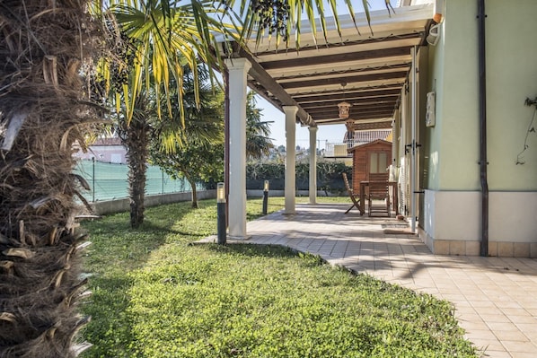 A covered outdoor area with palm trees, a tiled floor, and a view of the sea.