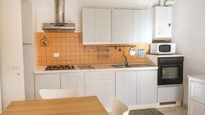 A compact kitchen with white cabinets, a stove, a microwave, and an oven. - M273 - Marcelli, new three-room apartment with garden (Marcelli)