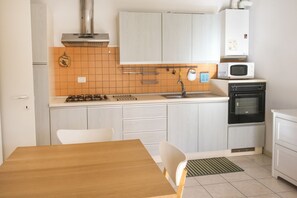 Une cuisine de taille réduite avec des meubles blancs, une cuisinière, un four à micro-ondes et un four traditionnel.