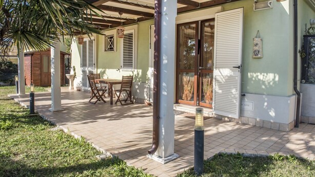 A covered patio area with a table and chairs, a door with a window, and a gas meter on the wall. - M273 - Marcelli, new three-room apartment with garden (Marcelli)