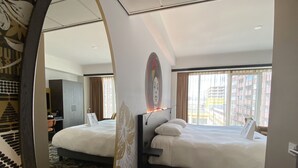 Hotelkamer met twee bedden, een bureau, een stoel en een groot raam met uitzicht op de stad.