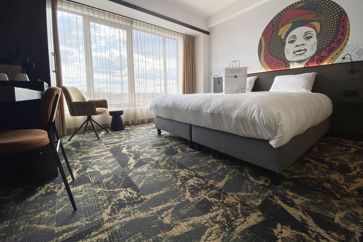 Ein Hotelzimmer mit Bett, Stuhl, Schreibtisch und großem Fenster.