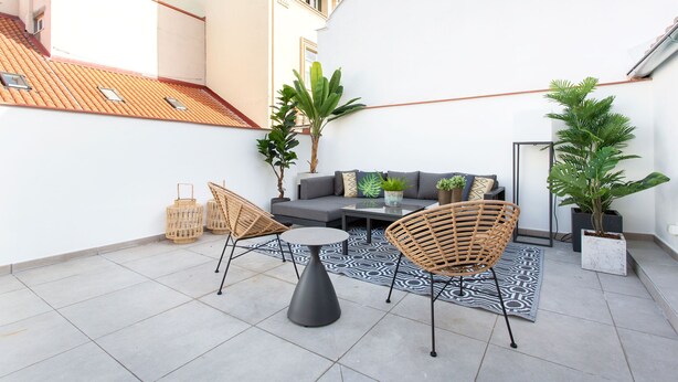 A small patio with a sofa, two wicker chairs, a round table, and potted plants.