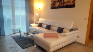 Una sala de estar moderna con un sofá blanco, una mesa de centro de vidrio y un cuadro de árboles en la pared.