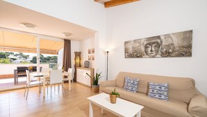 A modern living room with a sofa, a coffee table, and a dining area with chairs and a table. - Apartment Cala Anguilla  (Manacor Cala Anguila)