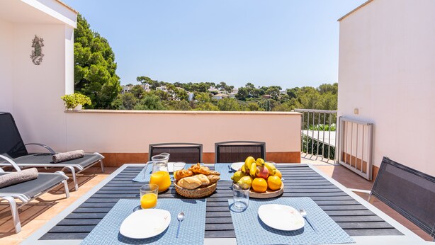 A terrace with a table set for breakfast, including bread, fruit, and juice. - Apartment Cala Anguilla  (Manacor Cala Anguila)