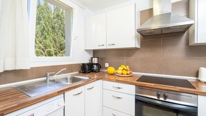 A modern kitchen with white cabinets, a built-in oven, and a window with a view of trees. - Apartment Cala Anguilla  (Manacor Cala Anguila)