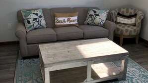 Uma sala de estar com um sofá cinzento, duas poltronas e uma mesa de centro.