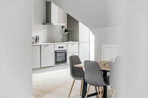 A modern kitchen with white cabinets, a built-in oven, and a dining area with two chairs and a table. - 175sqm High-end Luxury Apartment - Heart of CPH (Copenhagen)