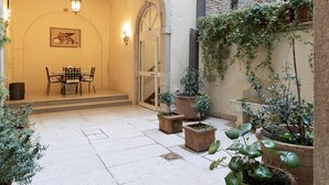 An outdoor patio area with a dining table and chairs, surrounded by potted plants and a stone wall. - Fortuny 3967 Luxury Suites Wine - Ve-l736-sanm3967at (Venice)