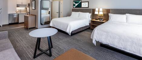 Una habitación de hotel con una cama, un escritorio, una silla, una mesita y una kitchenette.