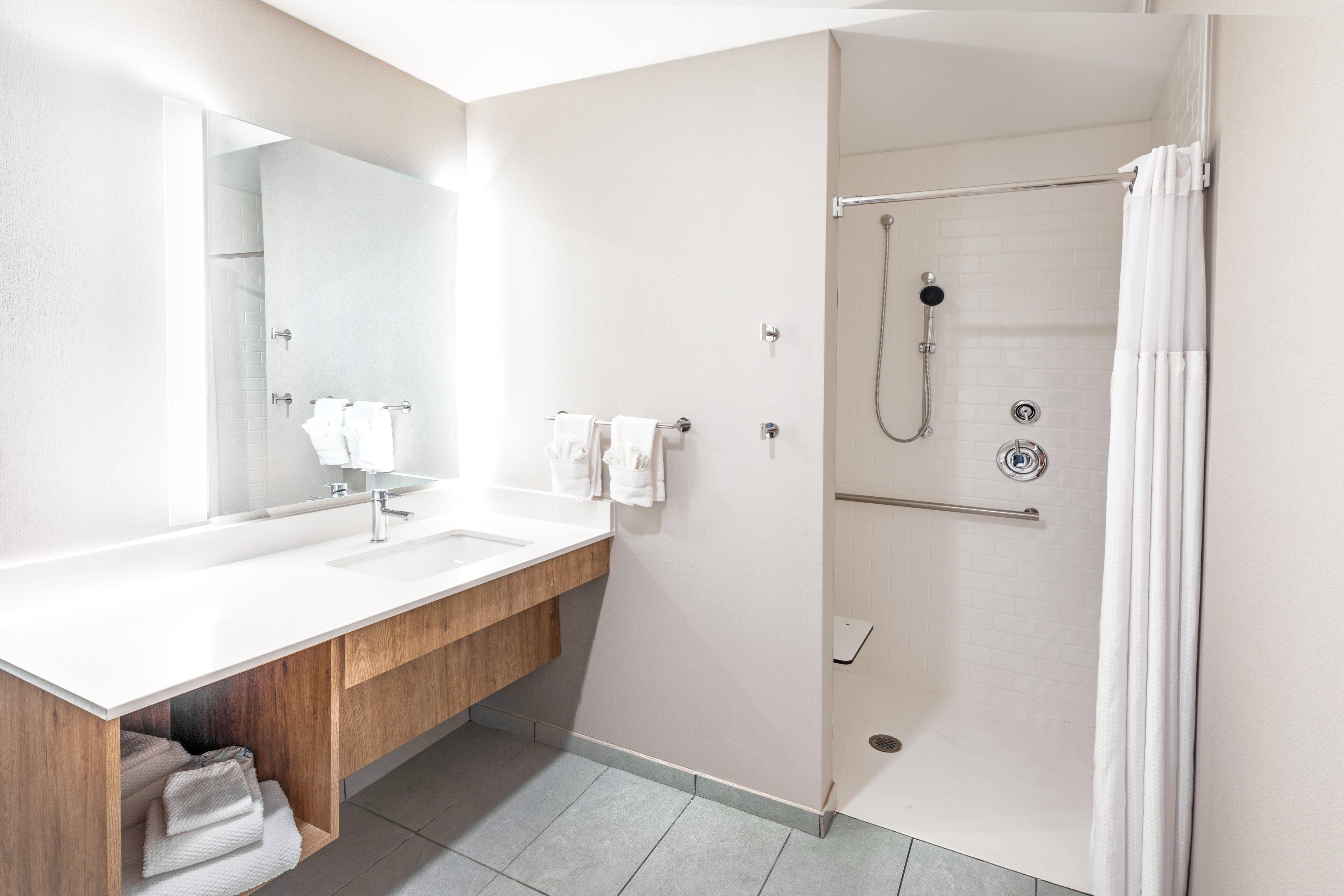 Un baño moderno con tocador de madera, un espejo grande, ducha con puerta de vidrio y cortina de ducha blanca.