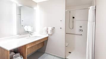 Un baño moderno con tocador de madera, un espejo grande, ducha con puerta de vidrio y cortina de ducha blanca.