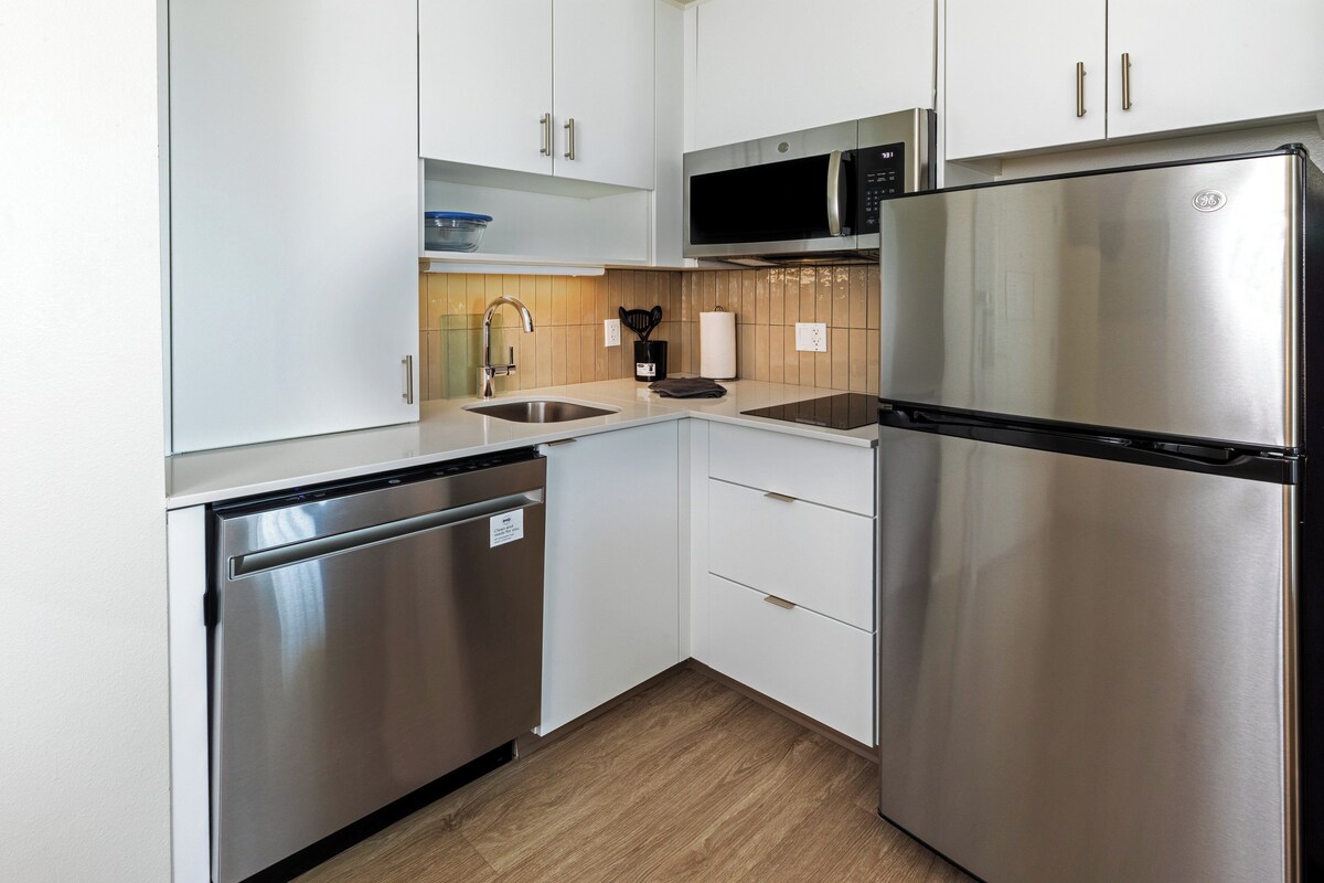 A modern kitchen with stainless steel appliances, white cabinetry, and a wooden floor.