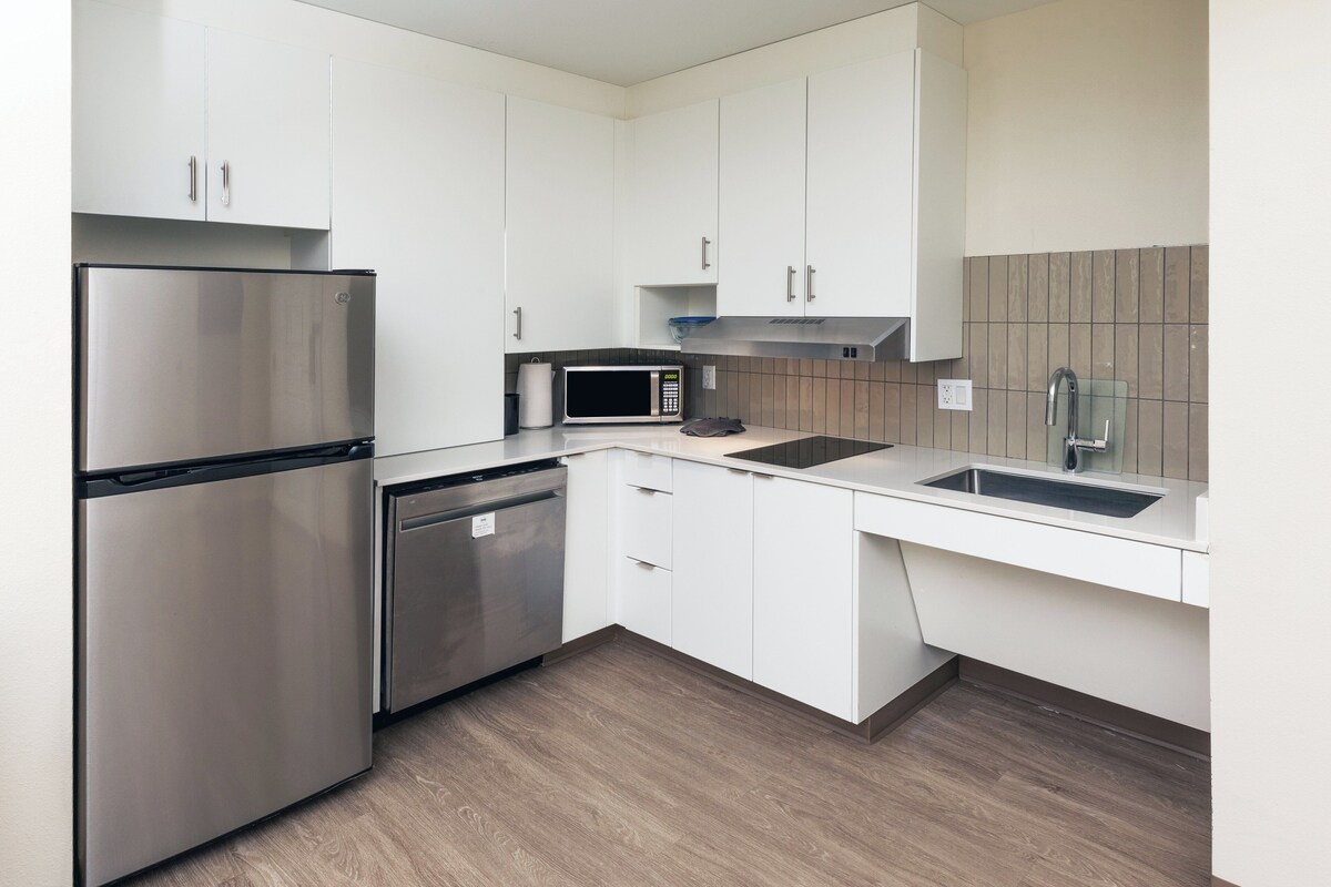 A modern kitchen with white cabinets, stainless steel appliances, a microwave, and a sink.