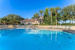 Une piscine avec des chaises longues, un bâtiment doté d’un toit en tuiles et des palmiers.