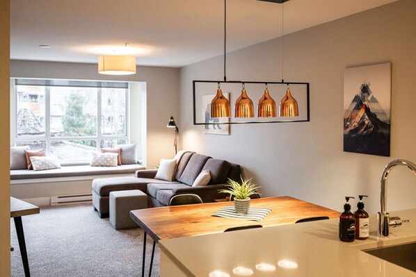 Un salon moderne comprenant un canapé, une table basse en bois, une plante en pot et un coin cuisine avec un évier et un plan de travail.