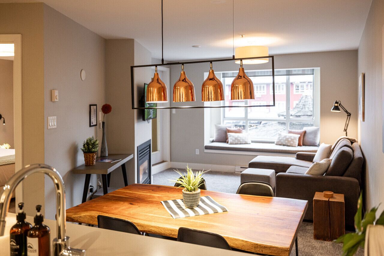 A modern living room with a wooden dining table, a sofa, and a window with a view of buildings.