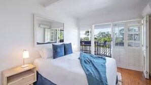 Une chambre avec un lit, une table de chevet, une grande fenêtre et un balcon.