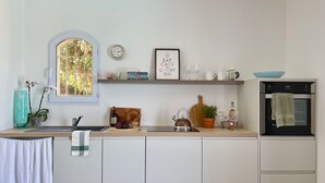A modern kitchen with white cabinetry, a window with a view, a kettle, a bookshelf, and a built-in oven. - Large stylish apartment with sea views over the Bay of Cannes and infinity pool (Les Adrets-de-l'Estérel)