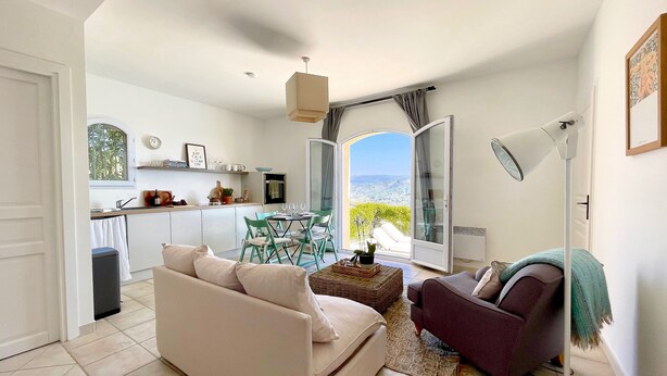 A modern living room with a sofa, armchair, and a dining table with chairs. There is a large window with a view of greenery and a door leading to a balcony. - Large stylish apartment with sea views over the Bay of Cannes and infinity pool (Les Adrets-de-l'Estérel)
