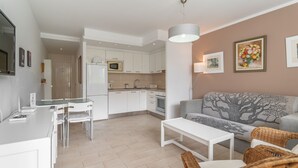 A modern kitchen with white cabinets, a dining area with a white table and chairs, and a living room with a grey sofa and wicker chairs. - GO2TENERIFE Apart'Arona City center & Beach at 5 min (Playa de las Américas)