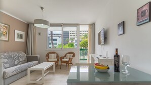 A modern living room with a sofa, two chairs, a glass table, and a balcony with a view of buildings and trees. - GO2TENERIFE Apart'Arona City center & Beach at 5 min (Playa de las Américas)