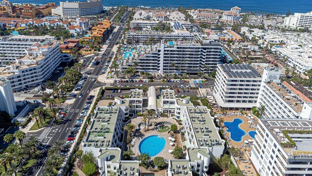 A high-rise hotel with multiple swimming pools, a central courtyard, and a view of the ocean. - GO2TENERIFE Apart'Arona City center & Beach at 5 min (Playa de las Américas)