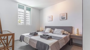 A modern bedroom with a large bed, bedside tables, a chair, and a window with a view of buildings.
